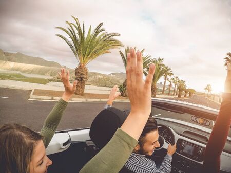 Happy friends having fun in convertible car on vacation - Young trendy people driving on cabriolet auto in summer road trip holidays - Transport and youth generation lifestyle conceptの写真素材