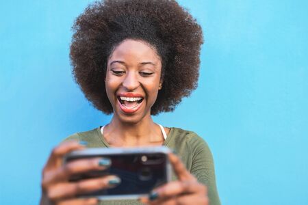 Young Afro woman using mobile smartphone - Happy African girl having fun with new trends technology apps - Youth millennial generation z and social influence concept - Blue backgroundの写真素材
