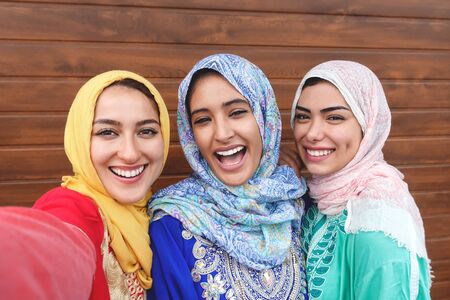 Happy Muslim girls taking selfie outdoor - Arabian young friends portrait making self photo for social media network - Religion culture and youth millennial lifestyle concept - Wooden backgroundの写真素材