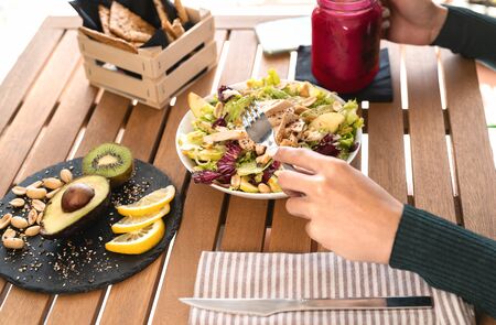 Female hands side view eating health vegetable salad with chicken breast avocado kiwi and drinking fresh smoothie fruits - Healthy nutrition food lifestyle conceptの写真素材
