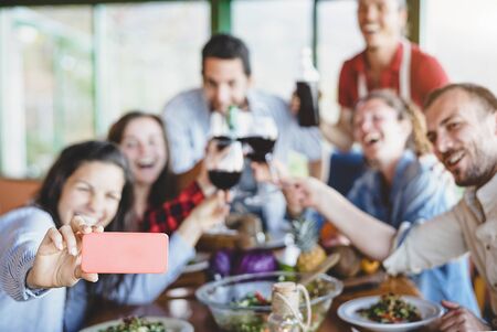 Group of happy friends taking selfie using mobile smart phone camera - Young millennial people having fun at dinner time - Friendship, food and drink, technology and youth lifestyle conceptの写真素材