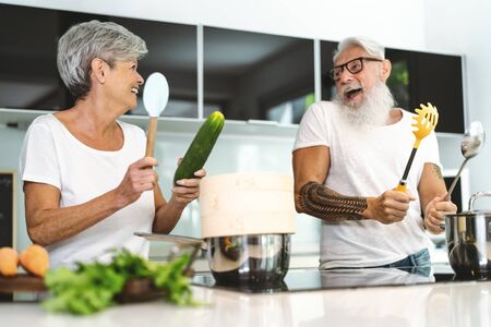 Happy senior couple having fun cooking together at home - Elderly people preparing lunch in modern kitchen - Retired lifestyle family time and food nutrition conceptの写真素材
