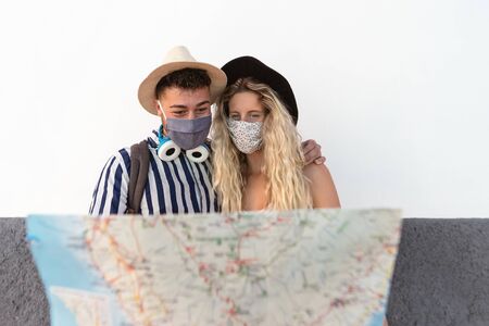 Young couple wearing face mask and holding travel map - Travelers people enjoying first trip after corona virus outbreak - Restart tourism and love relationship vacation lifestyle conceptの写真素材