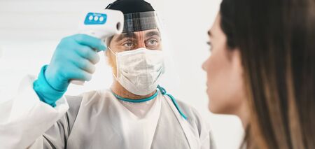 Doctor measuring temperature with new digital thermometer to young woman patient during corona virus pandemic - Health care and medical equipment conceptの写真素材