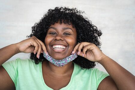 Happy Afro woman portrait - African girl wearing face mask smiling in front of camera - Health care...