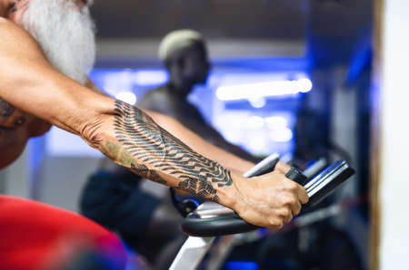 Senior man doing bike exercises in gym - Mature fit male training on cycling machine in health wellness center - Sport activity and fitness people lifestyle conceptの写真素材