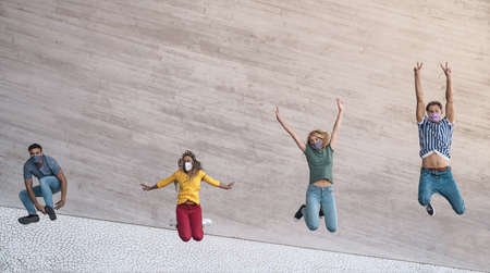 Young friends wearing face mask jumping outdoor - Happy people having fun in city after corona virus...