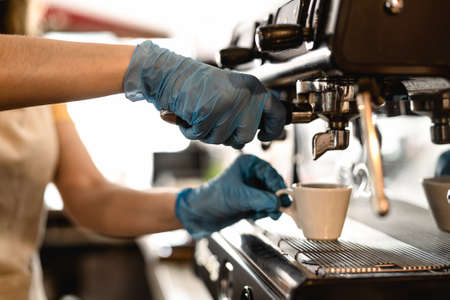 Young woman making coffee espresso while wearing surgical mask and gloves for preventing corona virus spread - Bar owner safety working - Hot beverages and covid-19 rules conceptの写真素材