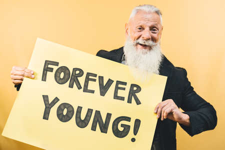 Happy youthful senior feeling forever young - Hipster mature man giving message with yellow banner - Elderly people lifestyle and positive emotions conceptの写真素材