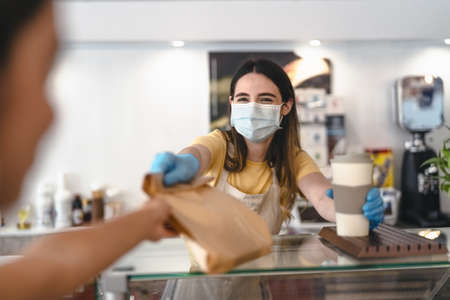 Bar owner working only with take away orders during corona virus outbreak - Young woman worker wearing face surgical mask giving takeout meal to customers - Healthcare and Food drink conceptの写真素材