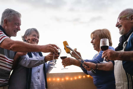 Happy senior friends dining and drinking red wine on house terrace - Mature people having fun laughing together at dinner party - Food and elderly friendship lifestyle conceptの写真素材