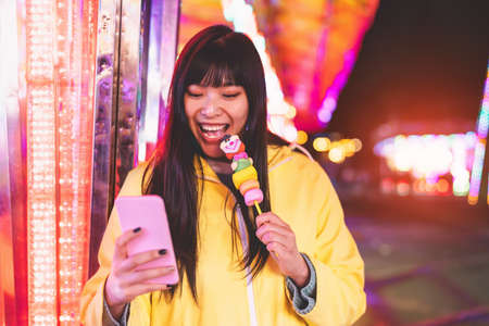 Asian girl taking selfie with mobile phone in amusement park - Happy woman having fun with new trends smartphone apps - Youth millennial people generation and social media addiction conceptの写真素材