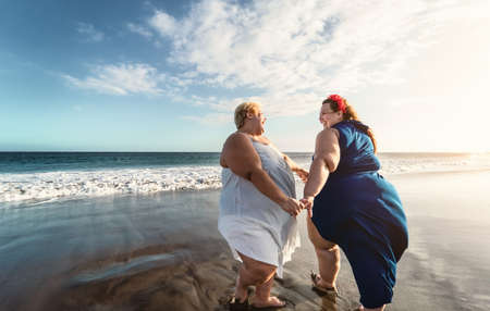 Happy plus size women dancing on the beach - Curvy overweight girls having fun during vacation in tropical destination - Over size confident people lifestyle conceptの写真素材