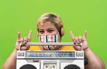 Plus size woman listening to music with wireless headphones and vintage boombox while wearing face...
