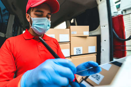 Delivery man wearing face protective mask to avoid corona virus spread - Young express courier working during coronavirus outbreak - Deliver and online buying conceptの写真素材