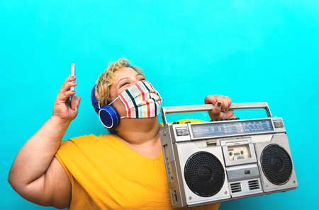 Happy plus size woman listening music with mobile smartphone and headphones while holding vintage...