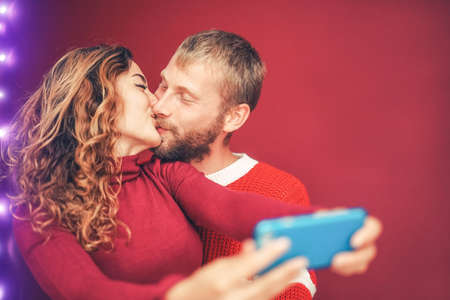 Happy couple taking selfie with mobile smartphone camera - Young romantic lovers kissing and celebrating Christmas holidays - Love relationship, xmas and technology trends conceptの写真素材