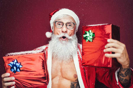Happy Santa Claus holding Christmas presents - Hipster bearded senior having fun wearing xmas clothes celebrating holidays - Elderly trendy people and traditional lifestyle cultureの写真素材