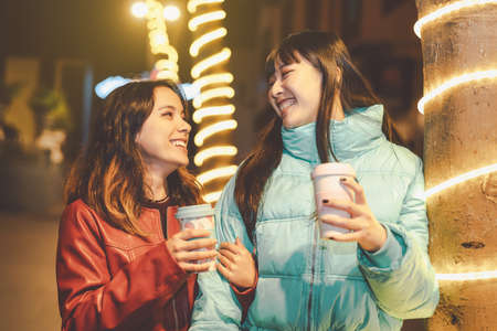 Happy friends walking in city while drinking coffee - Young girls having fun sharing time together outdoor - Friendship and youth people lifestyle conceptの写真素材