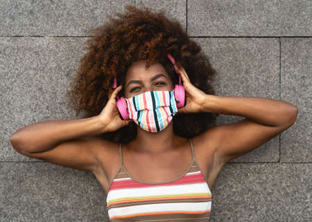 Happy Afro woman listening to playlist music with wireless headphones while wearing face colored...
