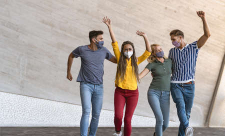 Young friends dancing together while wearing face mask outdoor - Happy people having fun in city...