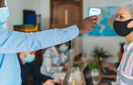 Young people in co-working creative space checkup temperature with digital thermometer while wearing face mask and keeping social distance to avoid corona virus spreadの写真素材