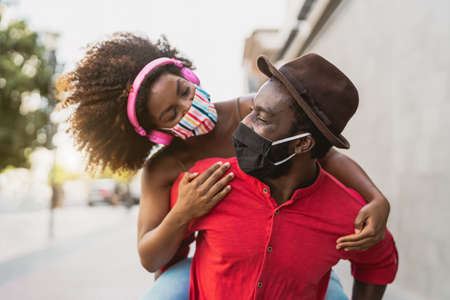 African couple piggyback wearing face mask - Happy Afro people having fun outdoor - Health care and youth relationship conceptの写真素材