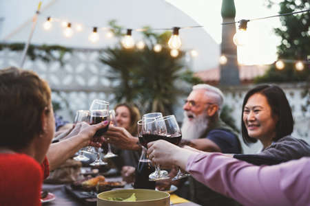 Happy family dining and tasting red wine glasses in barbecue dinner party - People with different ages and ethnicity having fun togetherの写真素材