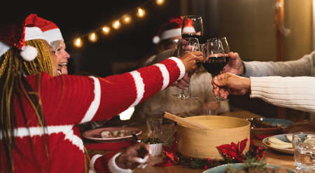 Happy multiracial senior friends toasting with red wine glasses during Christmas holidays dinner celebration on patio house partyの写真素材