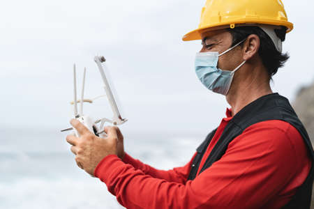Male engineer monitoring construction site using drone while wearing face mask during corona virus...