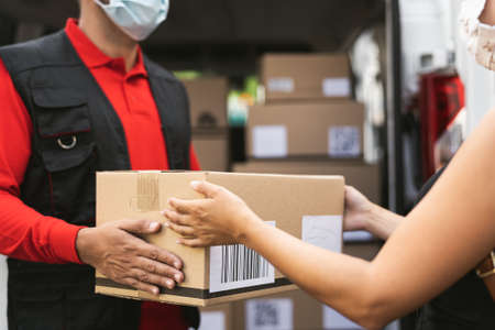 Delivery man wearing face protective mask to avoid corona virus spread - Young woman receiving an online order package from courier expressの写真素材