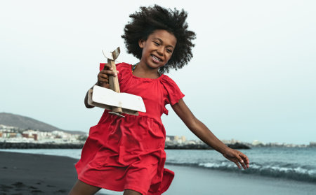 Afro child playing with wood toy airplane on the beach - Little kid having fun during summer holidaysの写真素材
