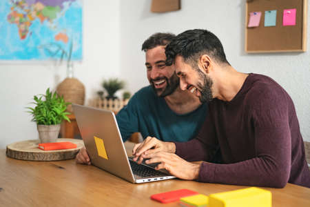 Gay men couple using laptop in living room at home - Homosexual love and gender equality in relationship conceptの写真素材