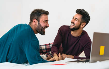 Happy gay men couple using laptop in bed - Homosexual love and gender equality in relationship conceptの写真素材
