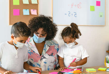 Teacher with children wearing face mask in preschool classroom during  virus pandemic - Healthcare and education conceptの写真素材