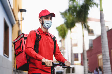 Rider man delivering meal with electric scooter in the city while wearing face mask during  virus outbreak - Ecological fast delivery food conceptの写真素材