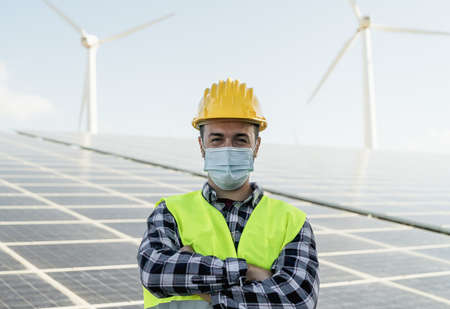 Young engineer working for alternative energy with wind turbine and solar panel while wearing face mask during   virus outbreak - Innovation and green power conceptの写真素材