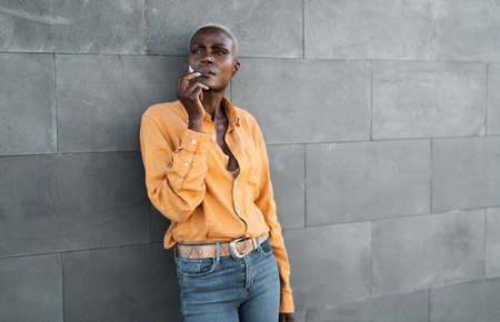 Afro senior woman smoking cigarette while standing against urban wallの写真素材