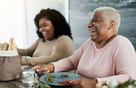 Happy black mother and daughter having fun eating healthy lunch at homeの写真素材