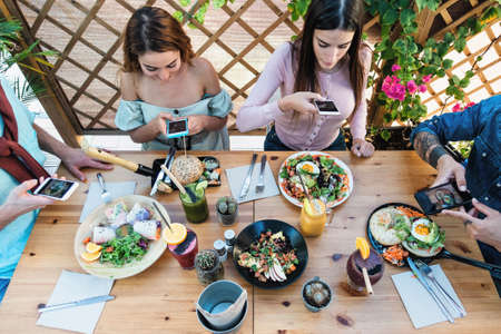 Young people taking food pictures with mobile smartphone to share on social media while having healthy meal in bar restaurant - Youth generation z and technology conceptの写真素材
