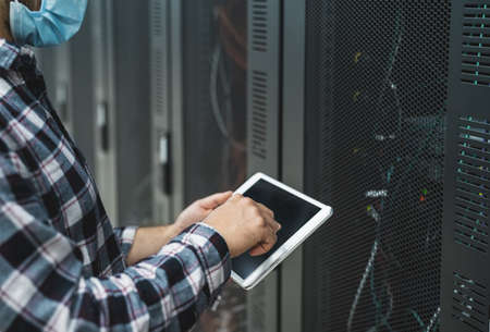 Male informatic engineer working inside server room database while wearing face mask during  virus...