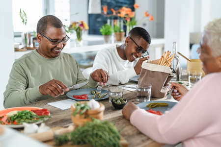 Happy afro Latin family eating healthy lunch with fresh vegetables at home - Food and parents unity conceptの写真素材