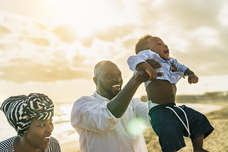 Happy African family having fun on the beach during summer holidays - Parents love concept