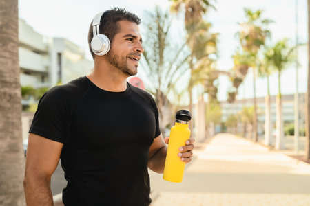 Latin man doing jogging and workout routine while listening music with wireless headphones outdoor