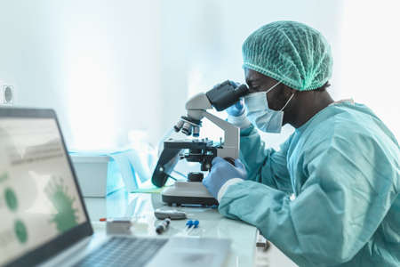 African doctor working in research lab examining microorganisms through microscope - Science and...