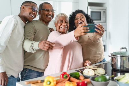 Happy Latin family having fun taking selfie with mobile smartphone while preparing healthy lunch in modern kitchen at home - Food and parents unity conceptの写真素材