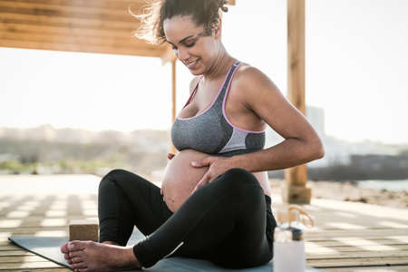 Young pregnant woman massaging the belly while doing yoga meditation outdoor - Health lifestyle and...