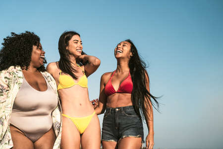 Happy multiracial females with different body size having fun walking on the beach during summer holidaysの写真素材