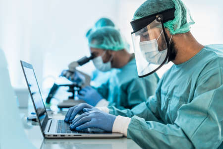 Doctors working in research laboratory using computer and examining microorganisms through microscope - Science and technology conceptの写真素材