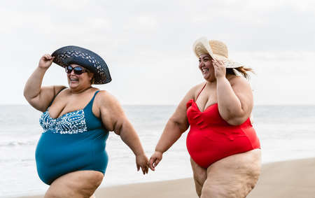 Happy plus size women having fun walking on the beach during summer vacations - Overweight people lifestyle conceptの写真素材